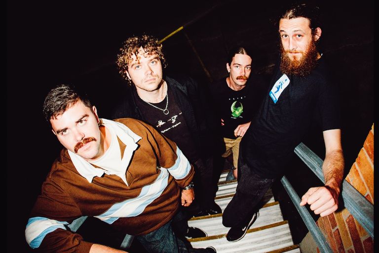 Indie rock band Concrete Surfers four members look up from a stairwell at night under harsh flash lighting, featuring a man with a full beard.